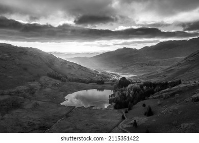 Black and white Epic aerial drone landscape image of sunrise from Blea Tarn in Lake District during stunning Autumn showing