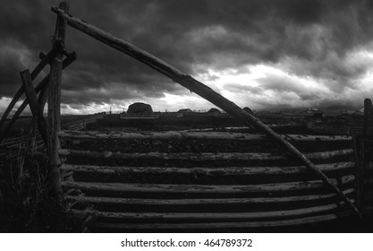 Black And White Fish Eye Close Up Of A Handmade Lodge Pole Gate In Cattle Country. Ultra Wide Angle With Sky Full Of Black Storm Clouds During Sunset With Some Bright Light Shining Through.