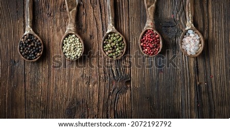 Black, white, green and red pepper and pink himalayan salt on an ceramic spoon over wooden backround