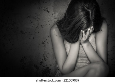 Black and white grunge image of a beautiful teenage girl sitting on the floor crying