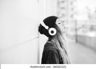 Black And White Half Length Profile Portrait Of Young Handsome Caucasian Blonde Hair Woman Leaning Against A Wall, Listening Music With Headphones, Eyes Closed - Serene, Enjoying, Music Concept