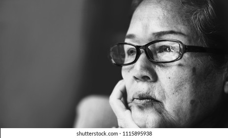 Black And White Image Of 60s Or 70s  Asian Elderly Woman Wearing Eyeglasses Rest Her Chin On Her Hands .She Looking Outside Or Flew Away.Sad Elderly Concept.