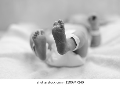 A black and white image of a baby lying on a changing mat in a hospital nursery wearing a nappy where the baby's feet are in focus immediately after a cesarean section.