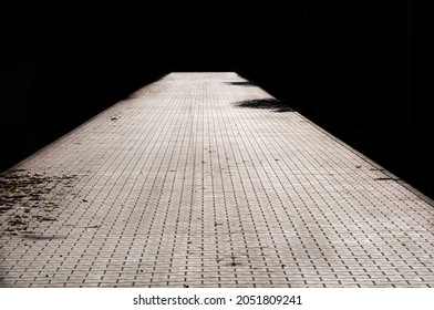 Black And White Image Of Brick Path Or Sidewalk With Perspective Going Into The Darkness, 
With Sunlight Reflecting Of The Bricks. 