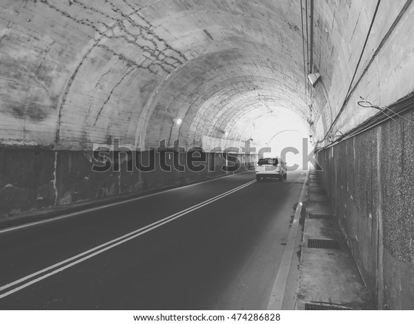 Black and white image of a car leaving a tunnel. Two\
people in the car.