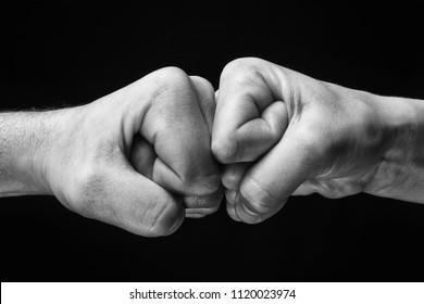 black and white image close up clash of two fists on black background. Concept of confrontation, competition etc.