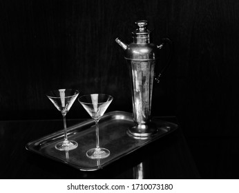 Black And White Image Of Cocktail Glasses And Antique Silver Decanter Claret Jug On A Silver Plate.