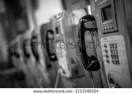 Black and white image of Coin-operated public payphone at a  railway station.