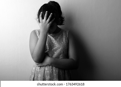 Black and white image of a disappointed girl placing her fingers on forehead. One light studio shot with shadow