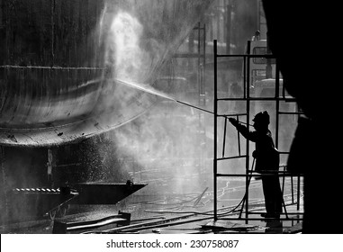 Black & white image of a dock worker steam cleaning a ships hull