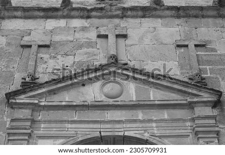 Black and white image of the facade of the door of a hermitage where crosses and skulls can be seen