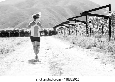 Black And White Image Of A Female Triathlete Running On A Trail On A Bright Sunny Day In The Vineyards Of The Western Cape Of South Africa