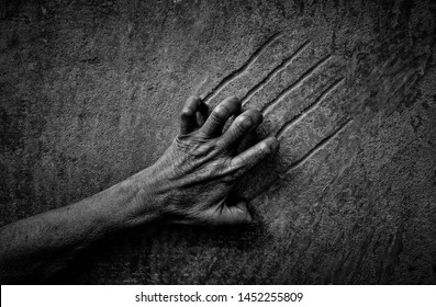 Black and white image of a hand scratching a wall. The concept of despair, hopelessness, pain, violence.