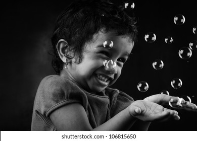 Black And White Image Of Happy Little Girl Playing With Bubbles