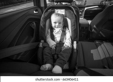 Black And White Image Of Happy Smiling Baby Boy Posing In Child Safety Car Seat