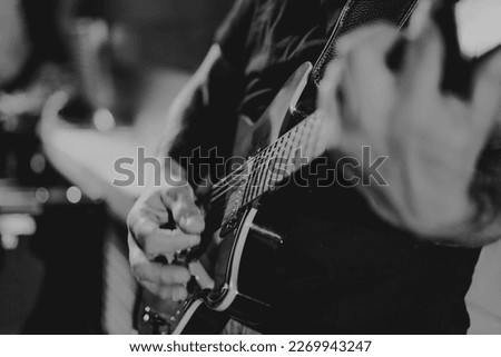 Black and white image of a man playing the electric guitar during a concert, no faces are shown, shallow depth of field