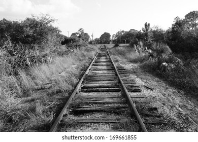 Black And White Image Of Old Railroad Train Track That Converges Into The Distance At A Street.