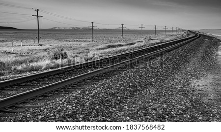 A black and white image of a railroad in the desert with a telegraph line and mountains in the backgroud.