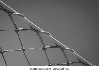 black and white image shows a close-up of a rope net, possibly part of a playground or a ship, against a smooth background. The net’s ropes are taut and intersecting at knots. - Powered by Shutterstock