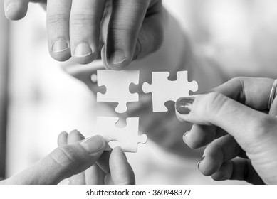 Black and white image of three people, male and female, holding puzzle pieces to match them. Conceptual of teamwork, cooperation and problem solving.
