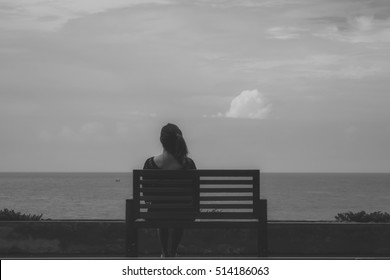 Black and white image of a woman sitting alone on a chair in front of the sea with feeling lonely