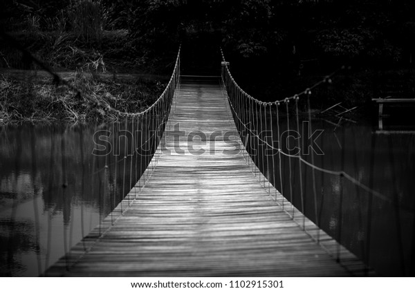 Black and white image of Wood and rope suspension\
bridge crossing the\
river.
