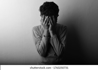 Black And White Image Of A Young Boy Feeling Shame Covering His Face With Hands.One Light Studio Shot With Shadow