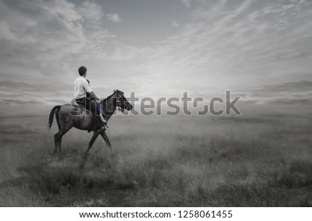 The black and white image of a young man practicing horseback riding in the light of the rising sun.