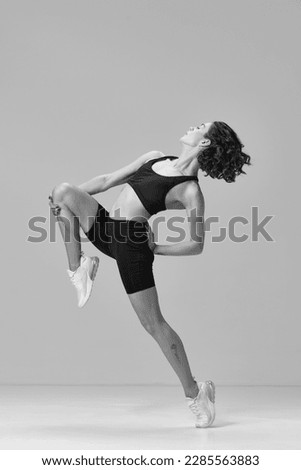 Black and white image. Young sportive woman in sportswear training, doing stretching exercises. Graceful movements. Concept of sportive lifestyle, beauty, body care, fitness, health