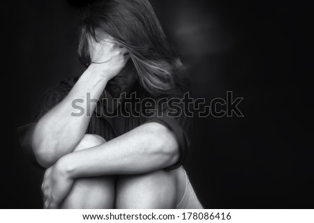 Black and white image of a young woman crying and covering her face useful to illustrate stress, depression or domestic violence