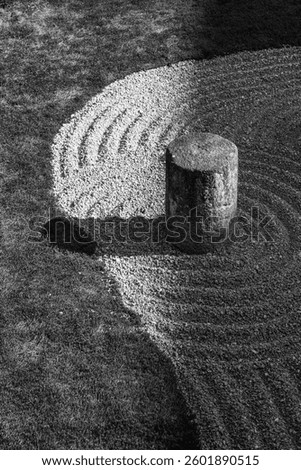 Black and white image of a Zen garden at a Japanese temple featuring a stone pillar casting a shadow on carefully raked gravel in concentric patterns.