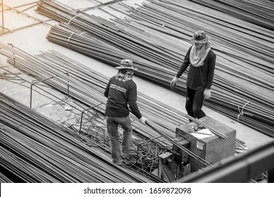 Black and white imahe of construction worker and many deformed steel bar working with hydraulic rebar cutting machine at the construction site. Large scale high rise building construction project.
