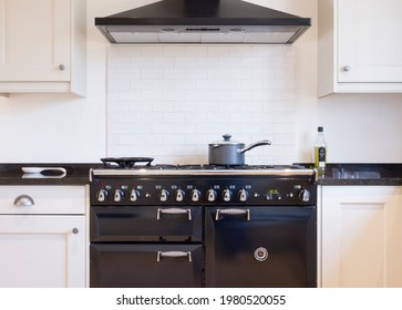 Black and white kitchen design. Painted wood modern kitchen with black enamel range cooker and chimney hood. UK shaker style kitchen remodeling
