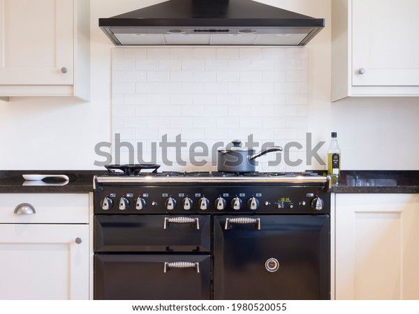 Black and white kitchen design. Painted wood\
modern kitchen with black enamel range cooker and chimney hood. UK\
shaker style kitchen\
remodeling