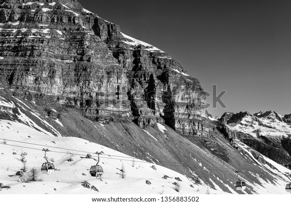 Black and white landscape. Cable car to sky resort.\
Massive rocks and mountains on the horizon. Winter holidays in the\
Alps