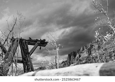 A black and white landscape featuring a rustic wooden structure, barren trees, and dramatic clouds over rocky mountains, evoking a sense of solitude and nature's beauty. - Powered by Shutterstock