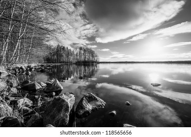 Black & white landscape with trees reaching to the sun over the lake