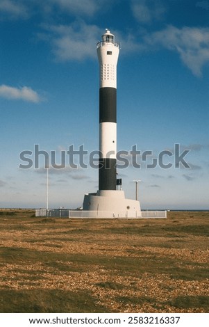 a black and white lighttower in the middle of shingle beach during sunny winter afternoon