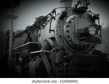 Black And White Low Angle Front View Of Steel 1800s Steam Train Engine Next To Railroad Signal