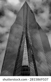 Black and white low angle view of a modern glass skyscraper reaching into dramatic cloudy sky, highlighting contemporary architecture and urban design.