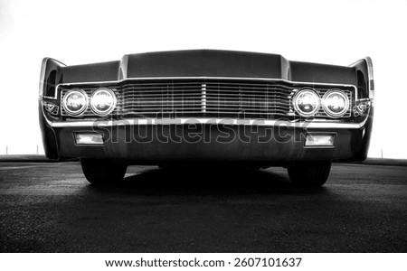Black and white low angle view of front grill of a vintage car with a white sky 
