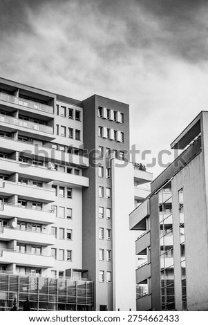 Black and white low angle view of modern residential apartment buildings with balconies and brick tower, dramatic cloudy sky