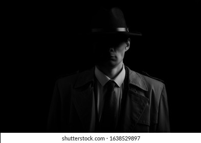 Black and white low key portrait of young gangster with hat in the darkness.