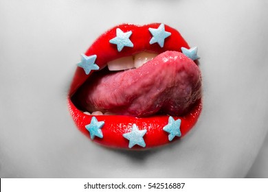 Black and white macro portrait of woman licking her lips painted red lipstick with candy in the form of stars.  