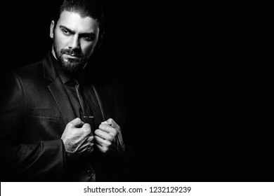 Black And White Male Portrait. A Man In A Black Classic Suit In A Black Shirt And Tie Over A Black Background. Dark-haired Young Man.