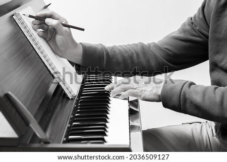 black and white male songwriter writing a song on music sheet while playing chord on acoustic piano keys. songwriting concept