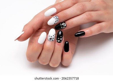 Black, white manicure with large and small dots, confetti, on long oval nails close-up on a white background.