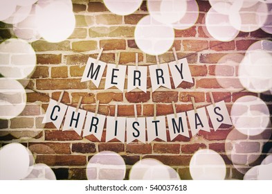 Black And White Merry Christmas Text Lettering Paper Handmade Garland, Blurred Lights Border Decoration On Brick Wall Background. Horizontal Greeting Letters Postcard, Instagram Look, Vintage Colors.