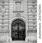 Black and white monochrome photo of a wrought iron gate to a mansion with carved stone ornaments 