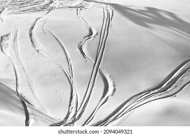 Black and white off-piste slope with track from ski and snowboard on sunny evening. View from above.
